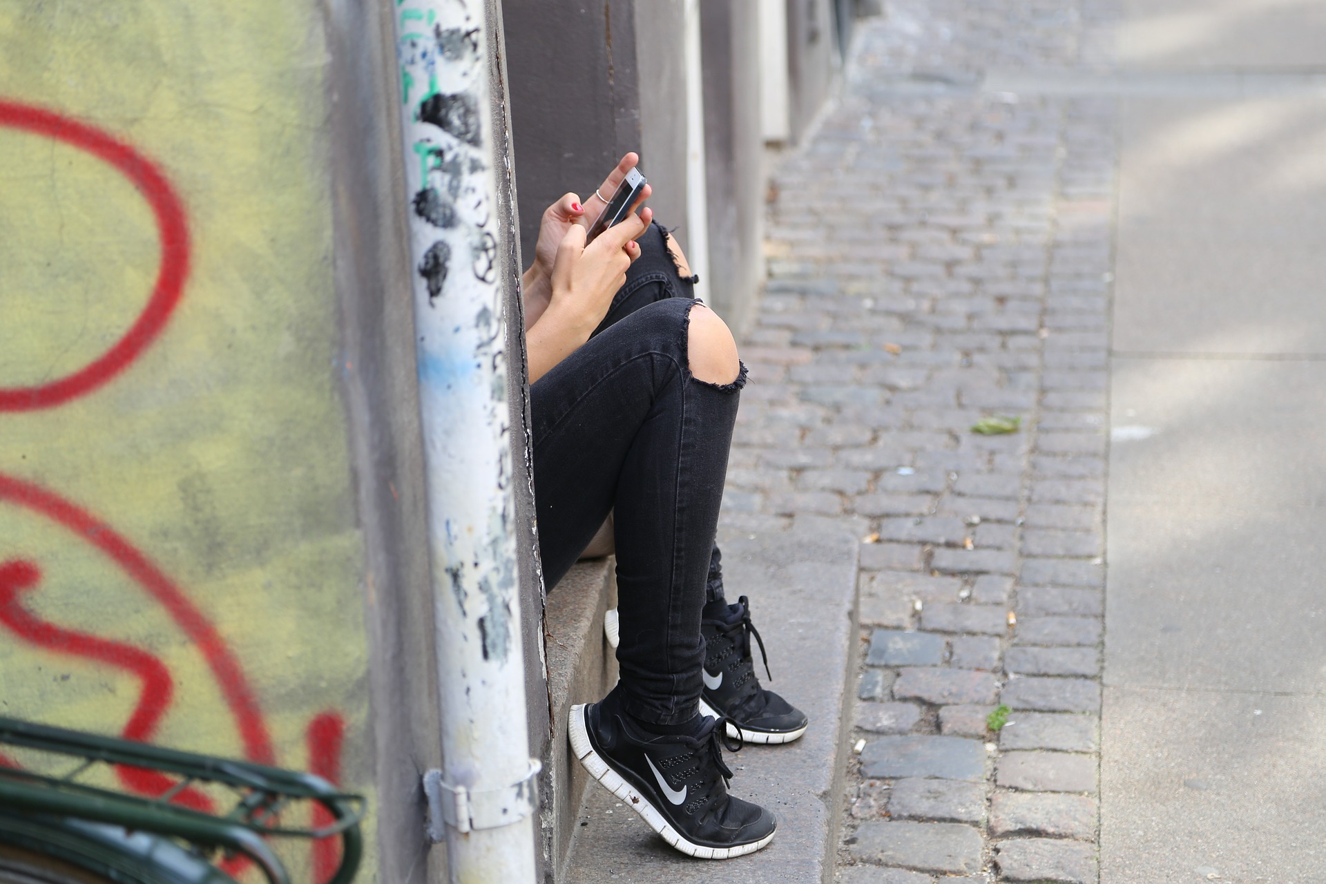 kollar på mobilen, trasiga byxor